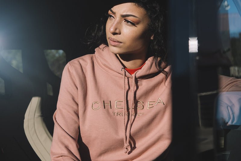 Angle View Of Female Model Sitting With A Dusty Pink with Gold Embroidery Hoodie 
